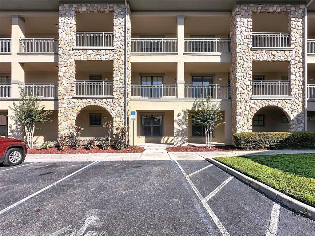 A three-story apartment building features stone-accented columns, balconies with metal railings, and a parking lot — 902 CHARO PARKWAY UNIT 622, DAVENPORT, FL
