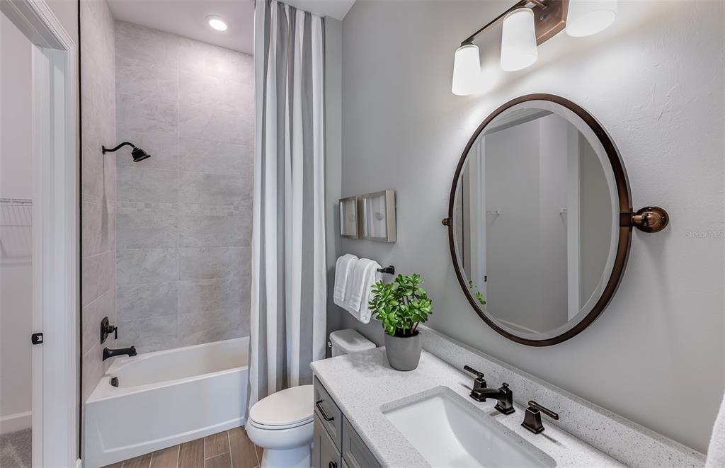 A bathroom features a gray vanity, a round mirror, and a tub-shower combo with tile — 1758 PEPPER GRASS DRIVE, NORTH PORT, FL