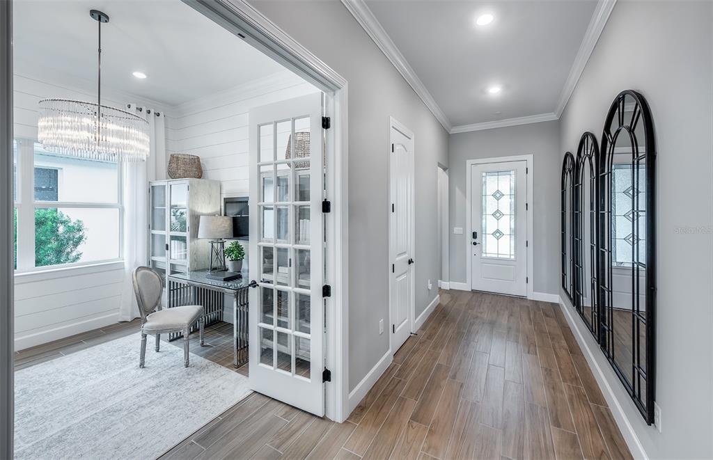 A home office with French doors opens into a hallway featuring wood-look tile and arched mirrors — 1758 PEPPER GRASS DRIVE, NORTH PORT, FL