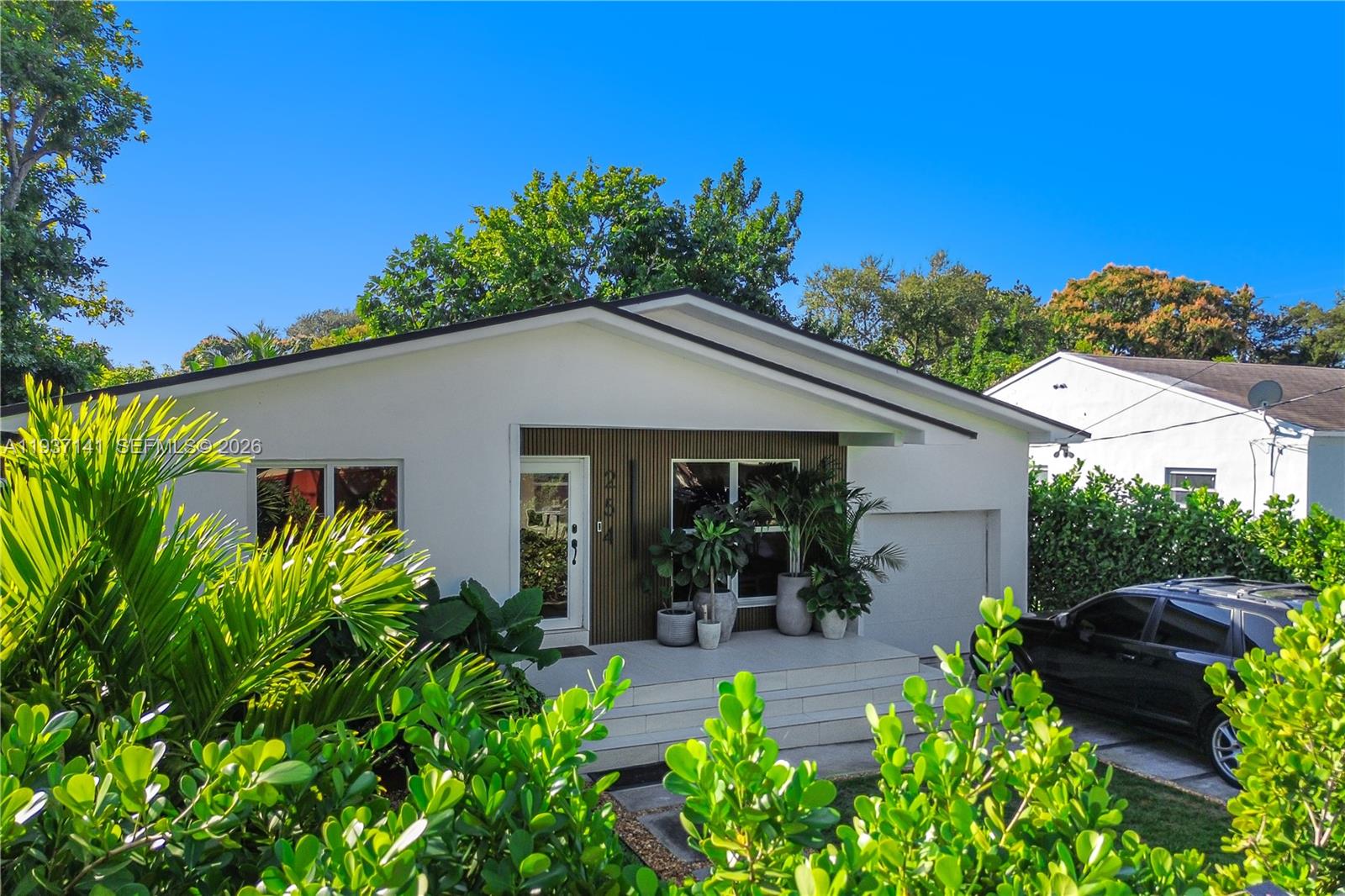 A single-story house with white stucco walls, a covered porch, and lush landscaping — 254 NW 43rd St, Miami FL 33127, MIAMI, FL