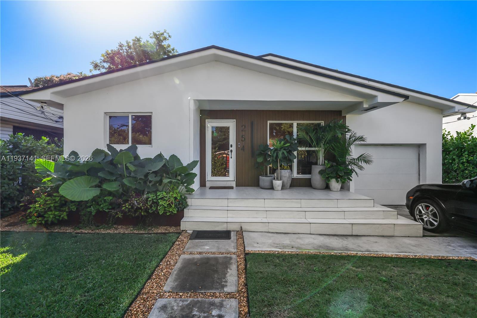 A white house features a tiled porch, wood-slat siding, and lush landscaping under a blue sky — 254 NW 43rd St, Miami FL 33127, MIAMI, FL