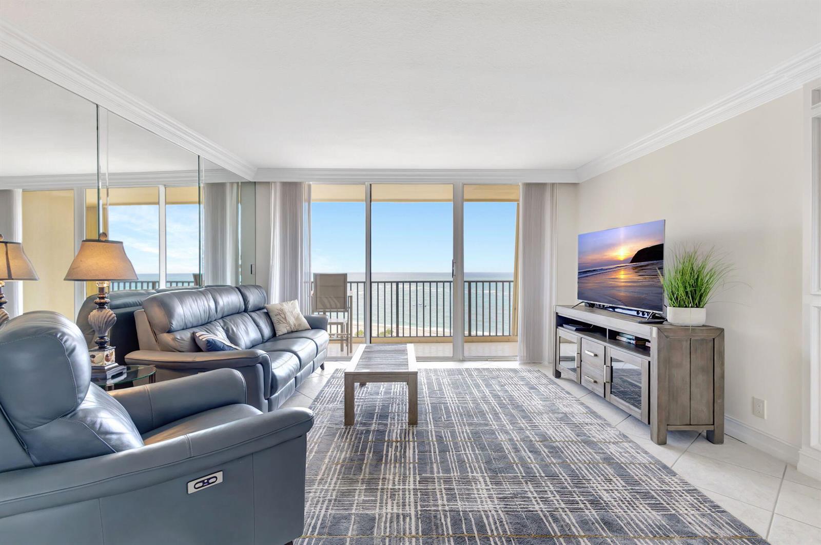 A living room with blue leather furniture, a plaid rug, and a balcony overlooking the ocean — 300 Ocean Trail Way # 907, Jupiter FL 33477, JUPITER, FL