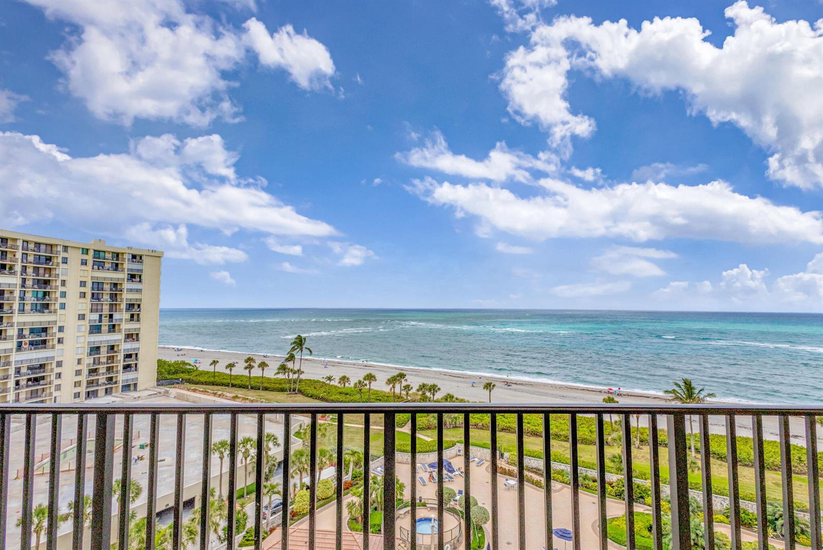 A high-angle view from a balcony overlooks a beach, the ocean, and a pool area — 300 Ocean Trail Way # 907, Jupiter FL 33477, JUPITER, FL