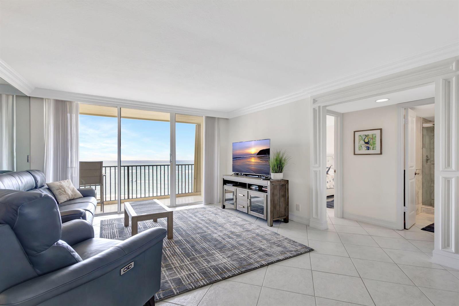 A living room with blue leather recliners, a patterned rug, and a balcony overlooking the ocean — 300 Ocean Trail Way # 907, Jupiter FL 33477, JUPITER, FL