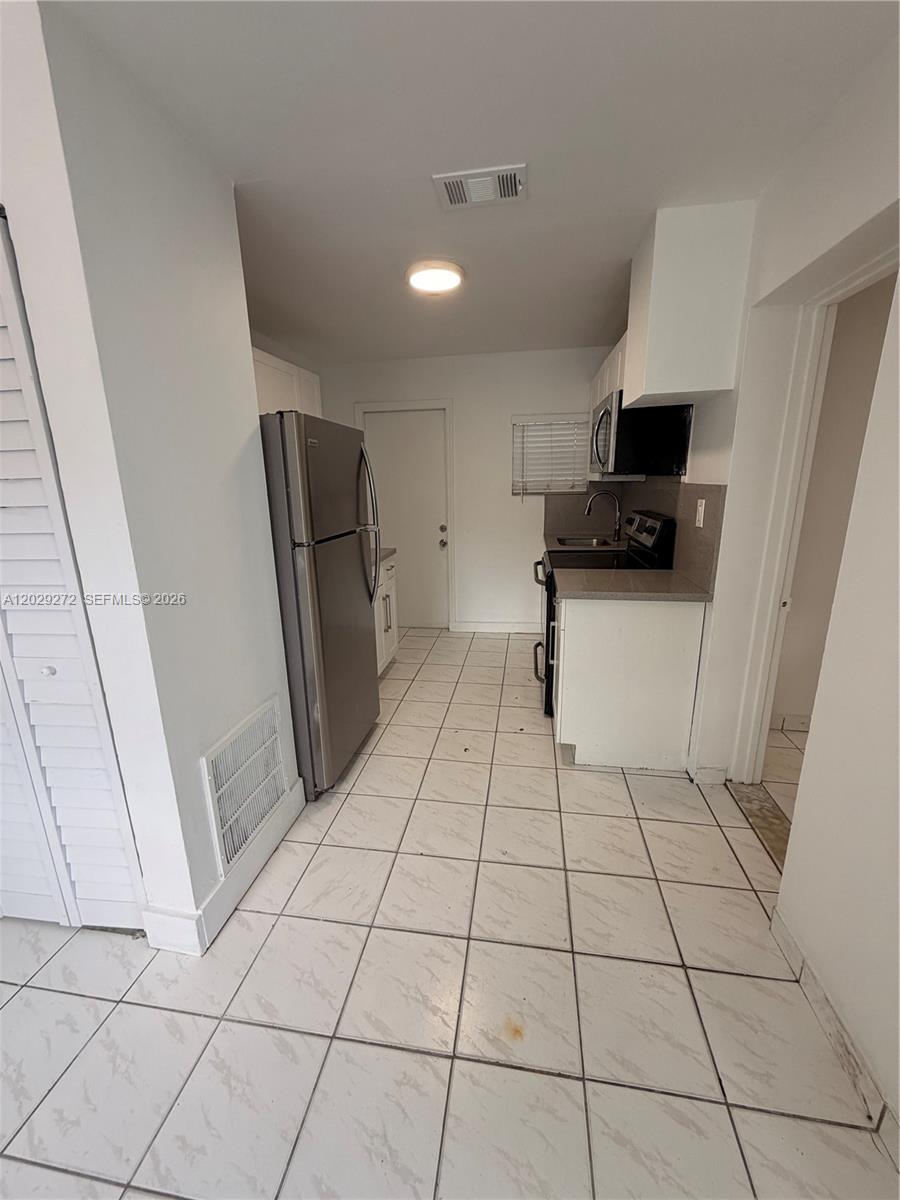 A kitchen features white cabinets, stainless steel appliances, and light-colored tile flooring — 2420 NW 31st St # 3, Miami FL 33142, MIAMI, FL