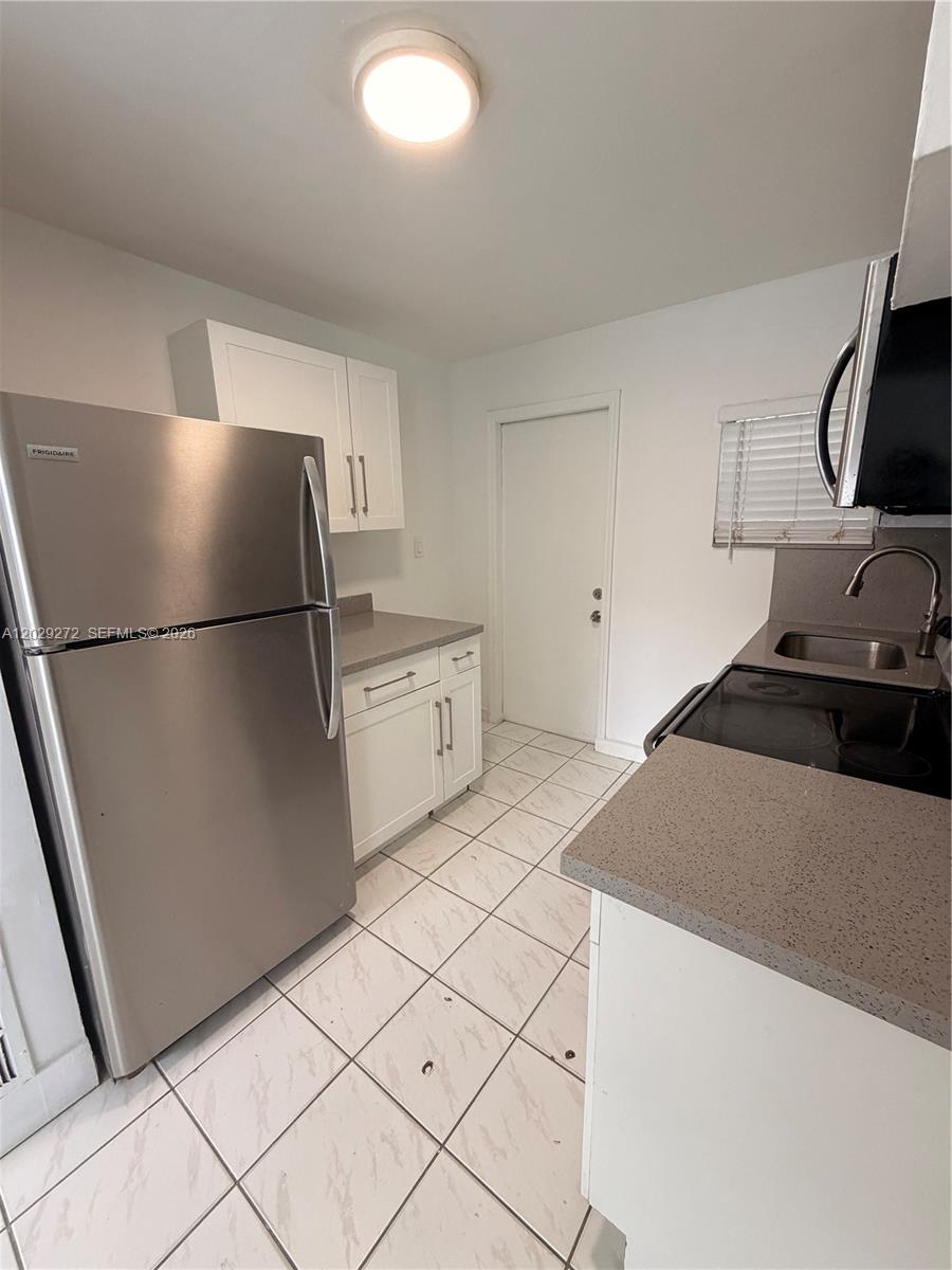 A small kitchen features white cabinets, stainless steel appliances, and light-colored tile flooring — 2420 NW 31st St # 3, Miami FL 33142, MIAMI, FL