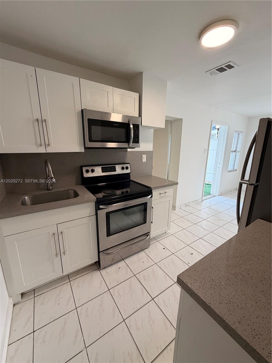 A kitchen features white cabinets, stainless steel appliances, gray countertops, and white tiled flooring — 2420 NW 31st St # 3, Miami FL 33142, MIAMI, FL