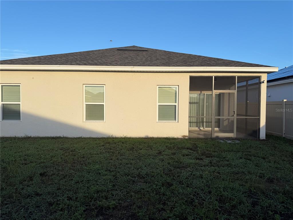 The exterior back view of a house features a screened-in porch and a vinyl fence — 2359 WHITE CEDAR WAY, HAINES CITY, FL