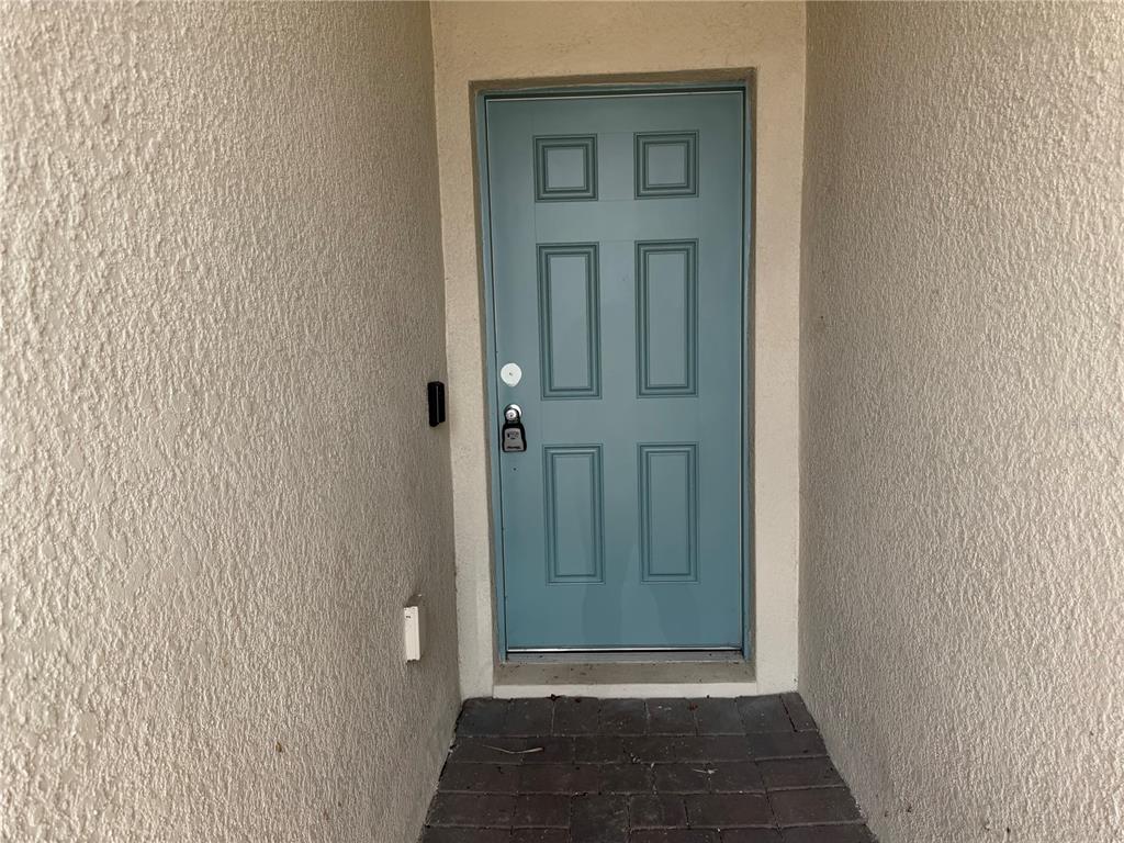 A blue six-panel front door is set within a recessed entryway with textured stucco walls — 2359 WHITE CEDAR WAY, HAINES CITY, FL