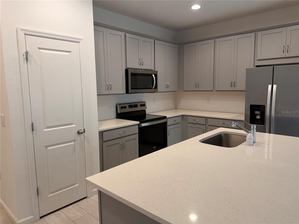 A kitchen features gray cabinets, stainless steel appliances, and a white quartz-topped island — 2359 WHITE CEDAR WAY, HAINES CITY, FL