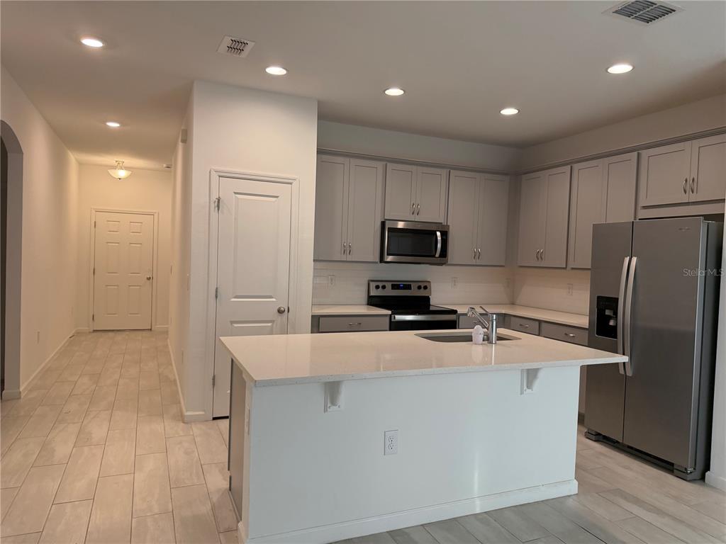 A kitchen with gray cabinets, stainless steel appliances, a white island, and light tile flooring — 2359 WHITE CEDAR WAY, HAINES CITY, FL