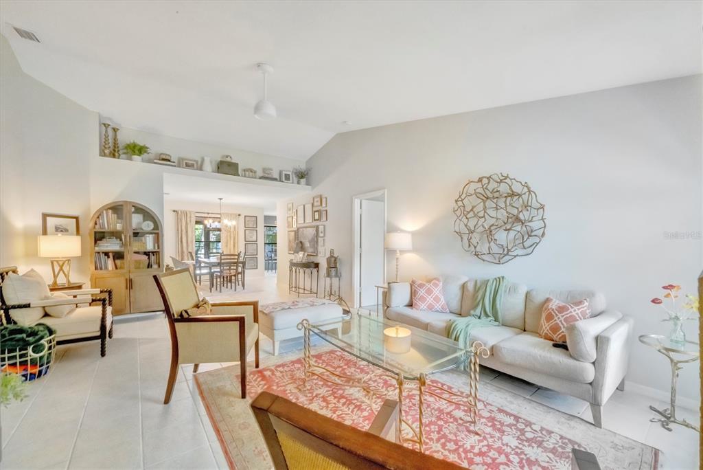 A living room with a vaulted ceiling, tiled floors, a glass coffee table, and area rug — 5872 PAUMA COURT, SARASOTA, FL