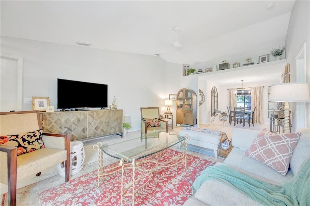 A living room with a glass coffee table, red rug, and a view into the dining area — 5872 PAUMA COURT, SARASOTA, FL