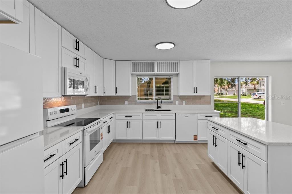 A bright kitchen features white cabinets, light countertops, a kitchen island, and light wood flooring — 1537 MORNING STAR DRIVE, CLERMONT, FL