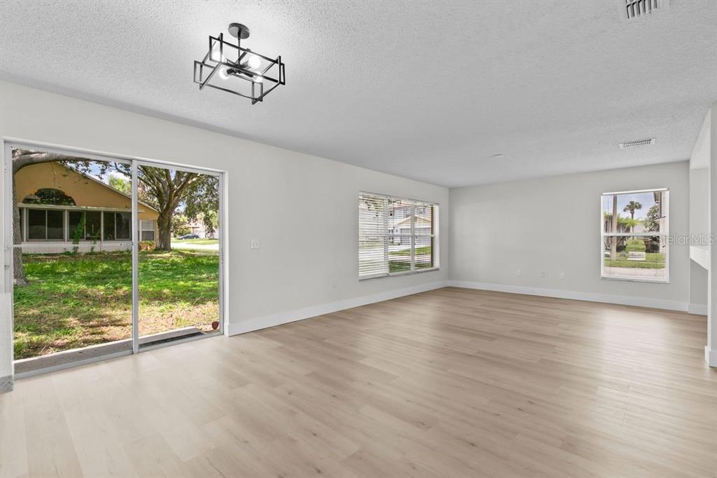 A bright living room features light wood-look flooring, white walls, a modern light fixture, and windows — 1537 MORNING STAR DRIVE, CLERMONT, FL