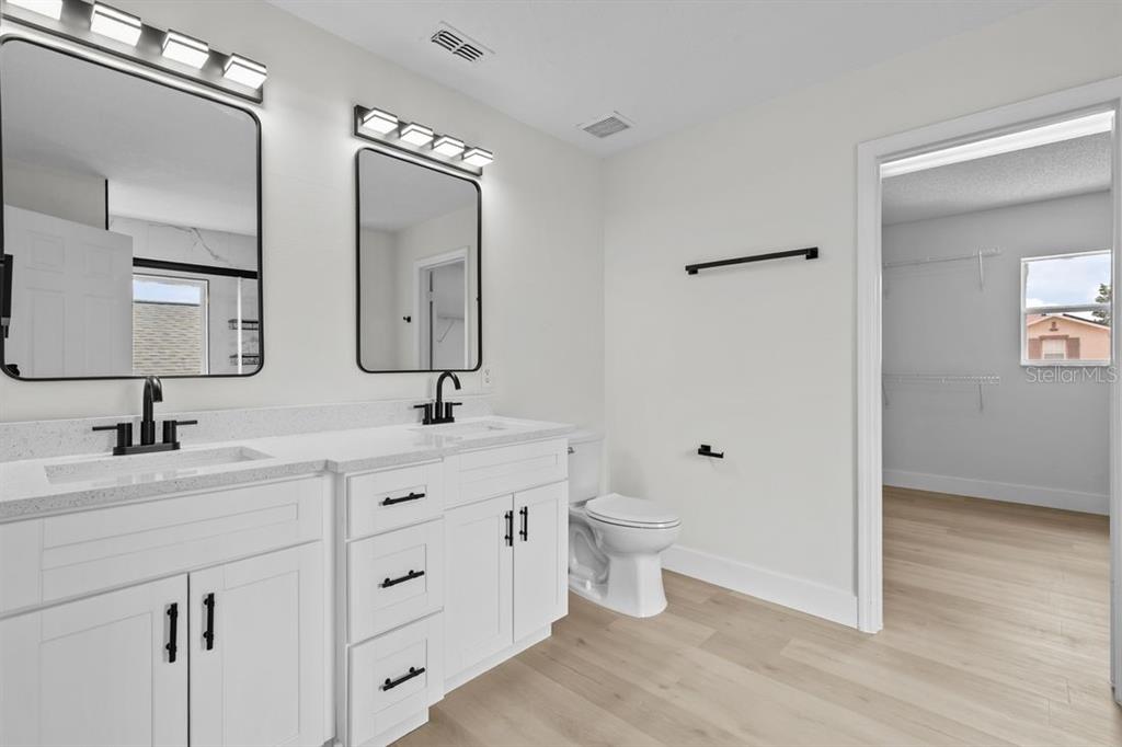 A modern bathroom features a double vanity with white cabinets, black hardware, and light flooring — 1537 MORNING STAR DRIVE, CLERMONT, FL