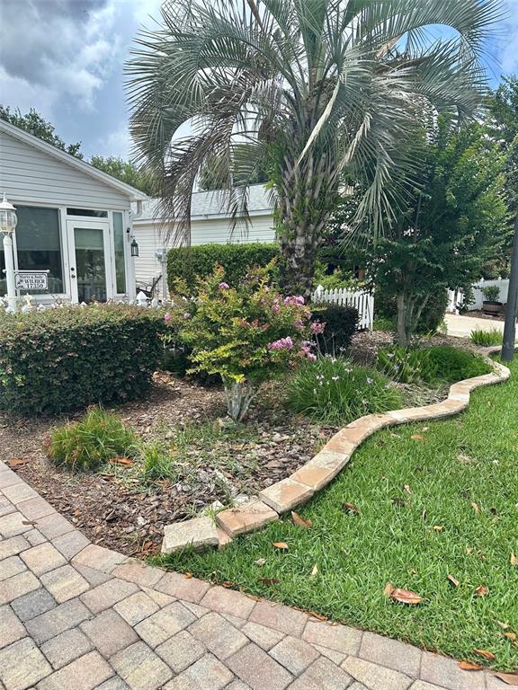 A landscaped front yard features a palm tree, flowering shrubs, and a stone-edged garden bed — 17350 SE 77TH SYCAMORE AVENUE, THE VILLAGES, FL
