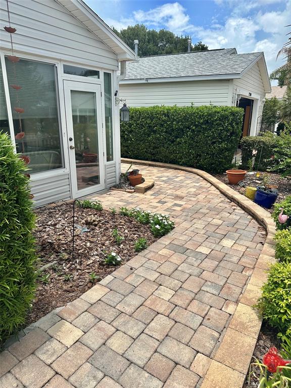 A paved walkway leads past a house exterior with a glass door and landscaping — 17350 SE 77TH SYCAMORE AVENUE, THE VILLAGES, FL
