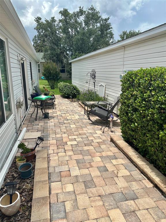 A paved patio sits between two white-sided buildings with outdoor furniture and a large hedge — 17350 SE 77TH SYCAMORE AVENUE, THE VILLAGES, FL