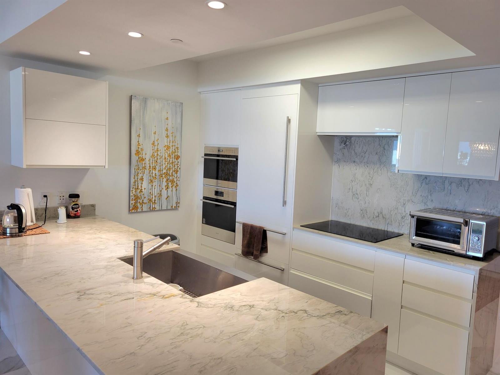 A modern kitchen features white cabinetry, marble countertops, a stainless steel sink, and built-in appliances — 1830 S Ocean Drive # 5111, FL 33009, FL