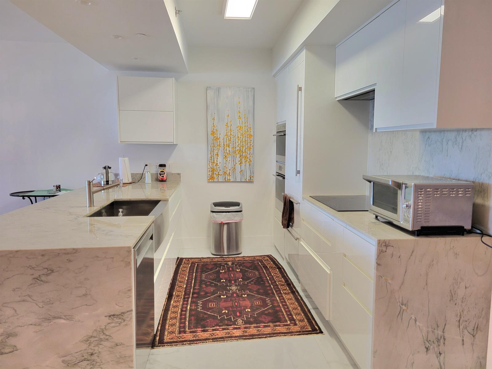 A modern kitchen features white cabinetry, marble countertops, a stainless steel sink, and a patterned rug — 1830 S Ocean Drive # 5111, FL 33009, FL