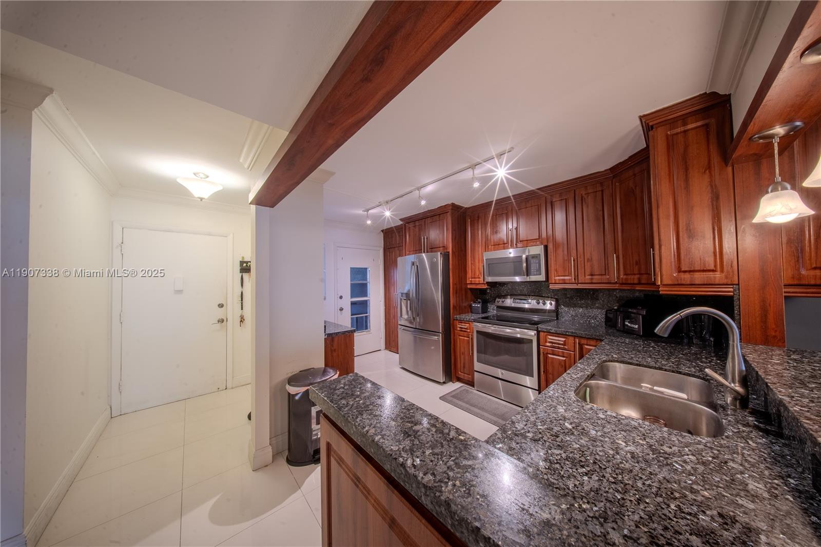 A kitchen features dark wood cabinets, granite countertops, stainless steel appliances, and tile flooring — 1660 NE 191st St # 1, Miami FL 33179, MIAMI, FL