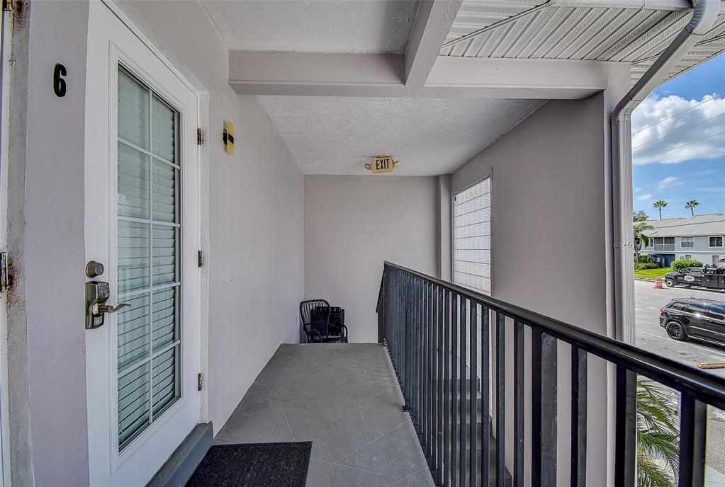 A covered outdoor walkway features a white door labeled number six and a black railing — 11975 3RD STREET E UNIT 6, TREASURE ISLAND, FL