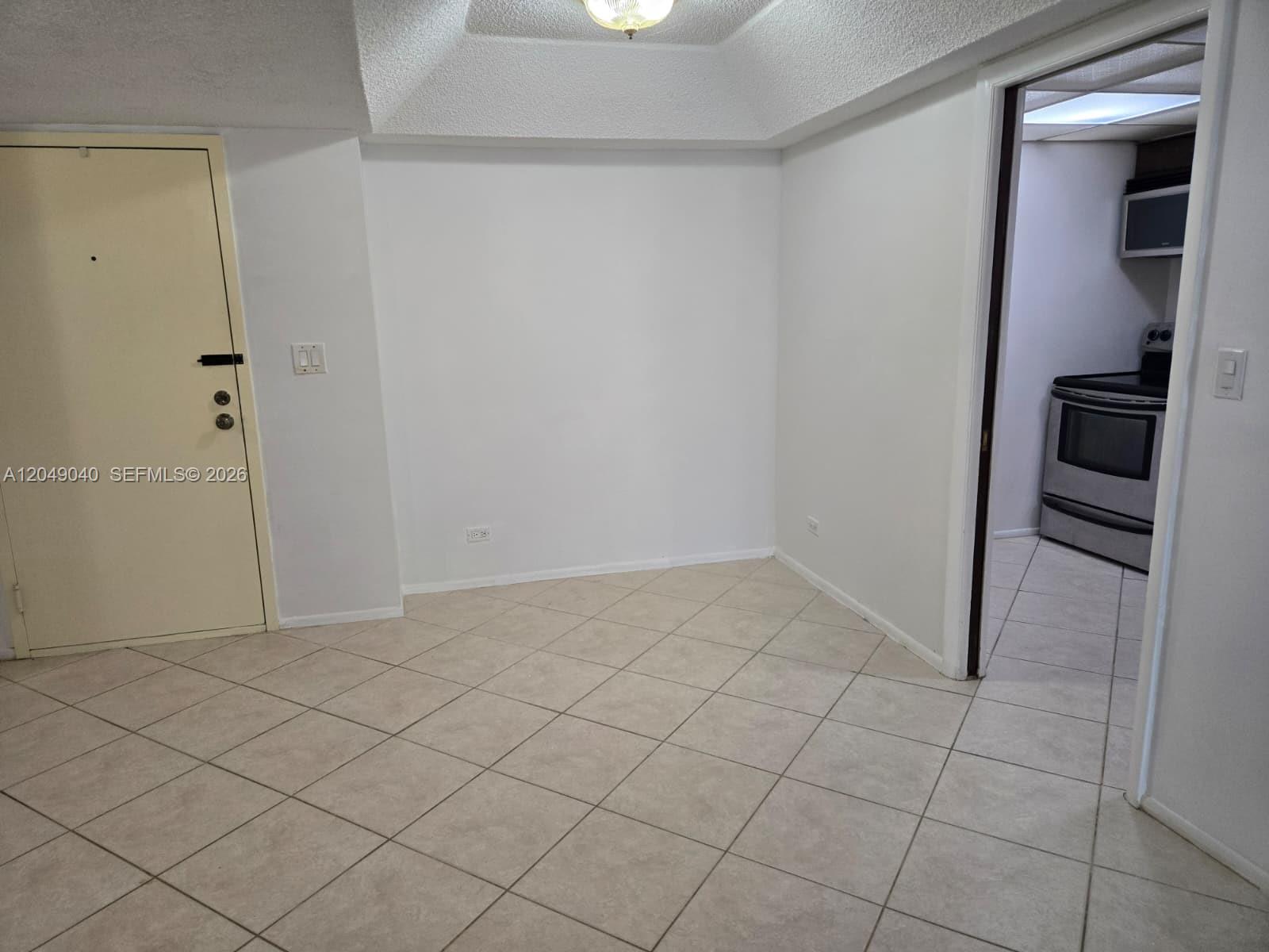 An empty room with tiled floors and a doorway leading to a kitchen — 3690 Inverrary Dr # 2Q, Lauderhill FL 33319, LAUDERHILL, FL