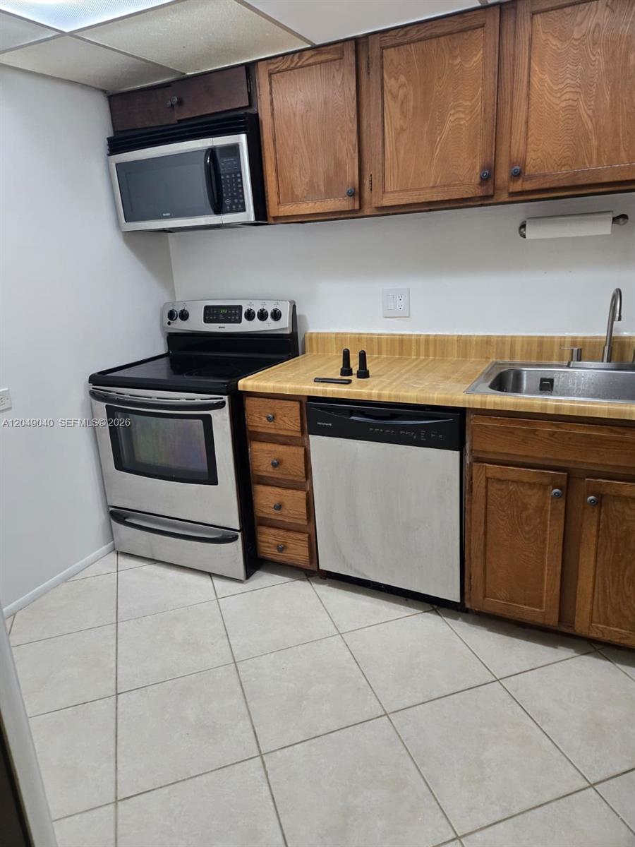 A kitchen features wood cabinets, stainless steel appliances, a laminate countertop, and tiled flooring — 3690 Inverrary Dr # 2Q, Lauderhill FL 33319, LAUDERHILL, FL