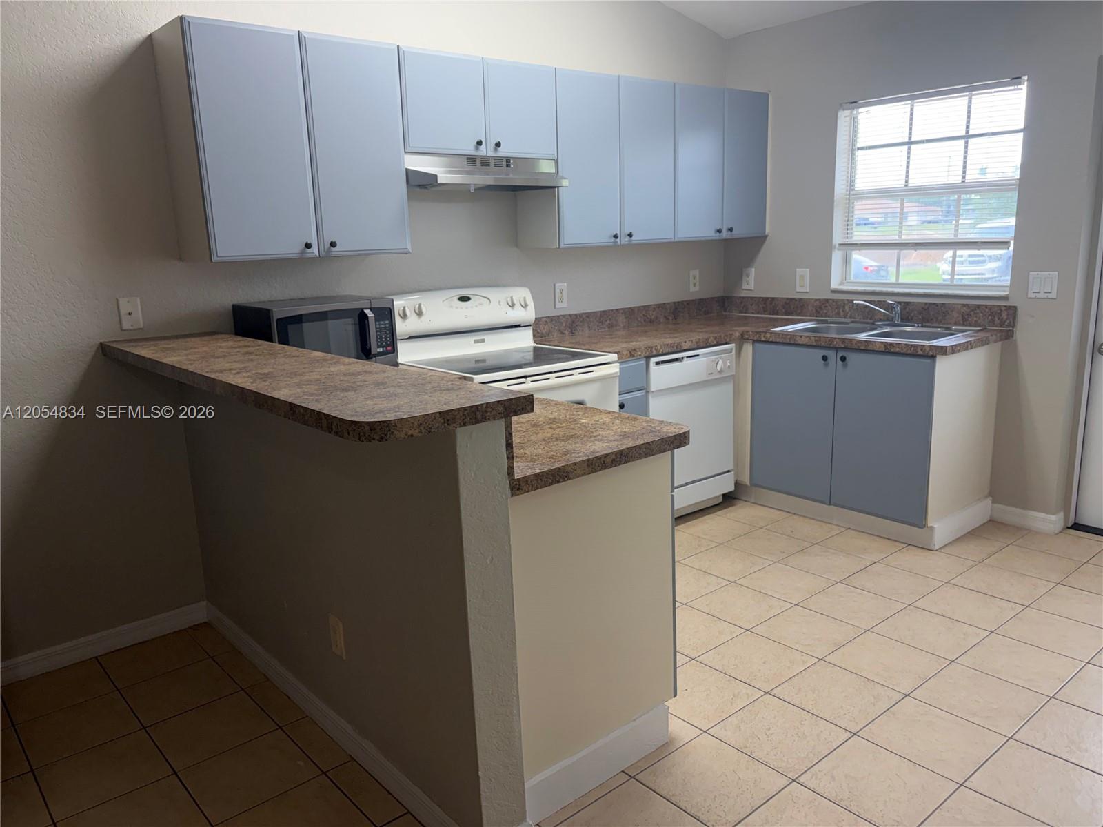 A kitchen features light blue cabinets, brown laminate countertops, white appliances, and tiled flooring — 4545 26TH ST SW # 0, Lehigh Acres FL 33973, LEHIGH ACRES, FL
