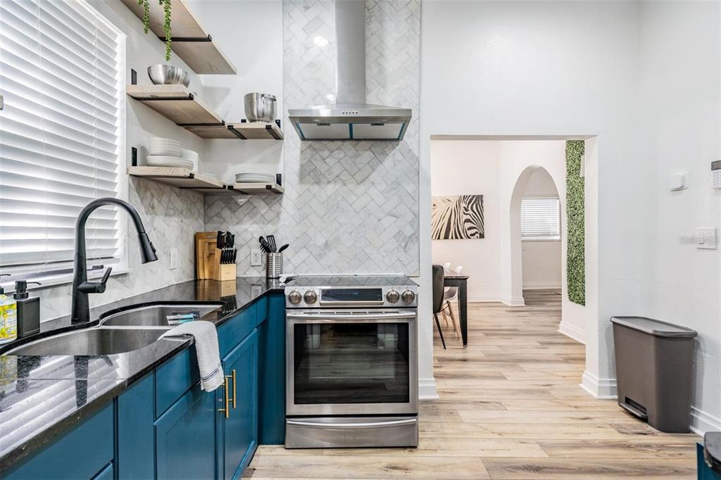 A kitchen features blue cabinets, a stainless steel stove, open shelving, and a herringbone backsplash — 2325 W GREEN STREET, TAMPA, FL