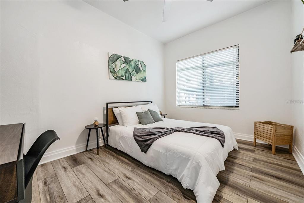 A bedroom features a bed with white bedding, wood-look flooring, and a window with blinds — 2325 W GREEN STREET, TAMPA, FL