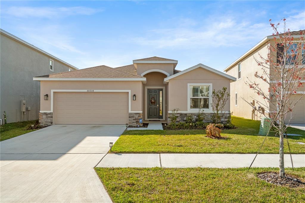 A single-story suburban house with a tan stucco exterior, stone accents, and a two-car garage — 32516 OSPREY PEAK WAY, SAN ANTONIO, FL