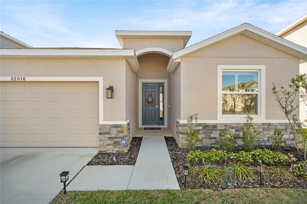 The exterior of a single-story house features a tan stucco facade, stone accents, and a garage — 32516 OSPREY PEAK WAY, SAN ANTONIO, FL