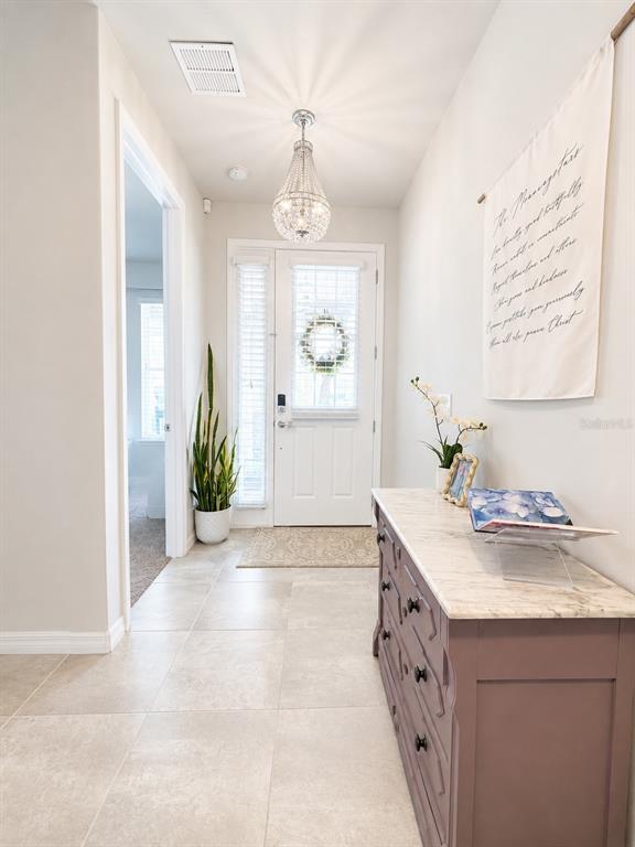 A bright entryway features tile flooring, a crystal chandelier, a white door, and a dresser — 8011 BUSHMASTER AVENUE, ORLANDO, FL