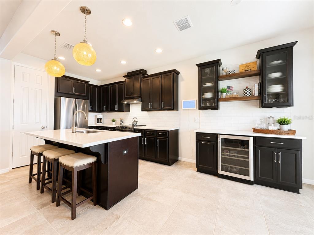 A kitchen features dark wood cabinetry, white countertops, a central island, and a wine cooler — 8011 BUSHMASTER AVENUE, ORLANDO, FL
