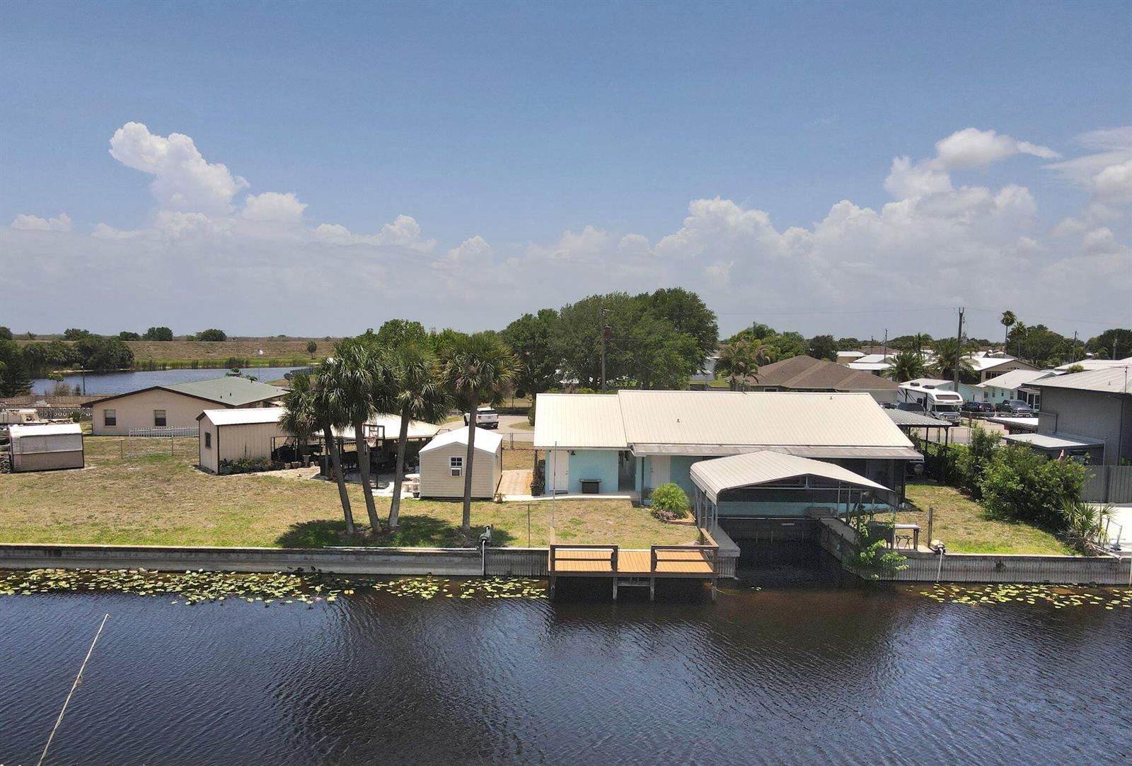 An aerial view of a waterfront house with a boat slip, dock, and storage sheds — 1115 Elm Street, Okeechobee FL 34974, OKEECHOBEE, FL