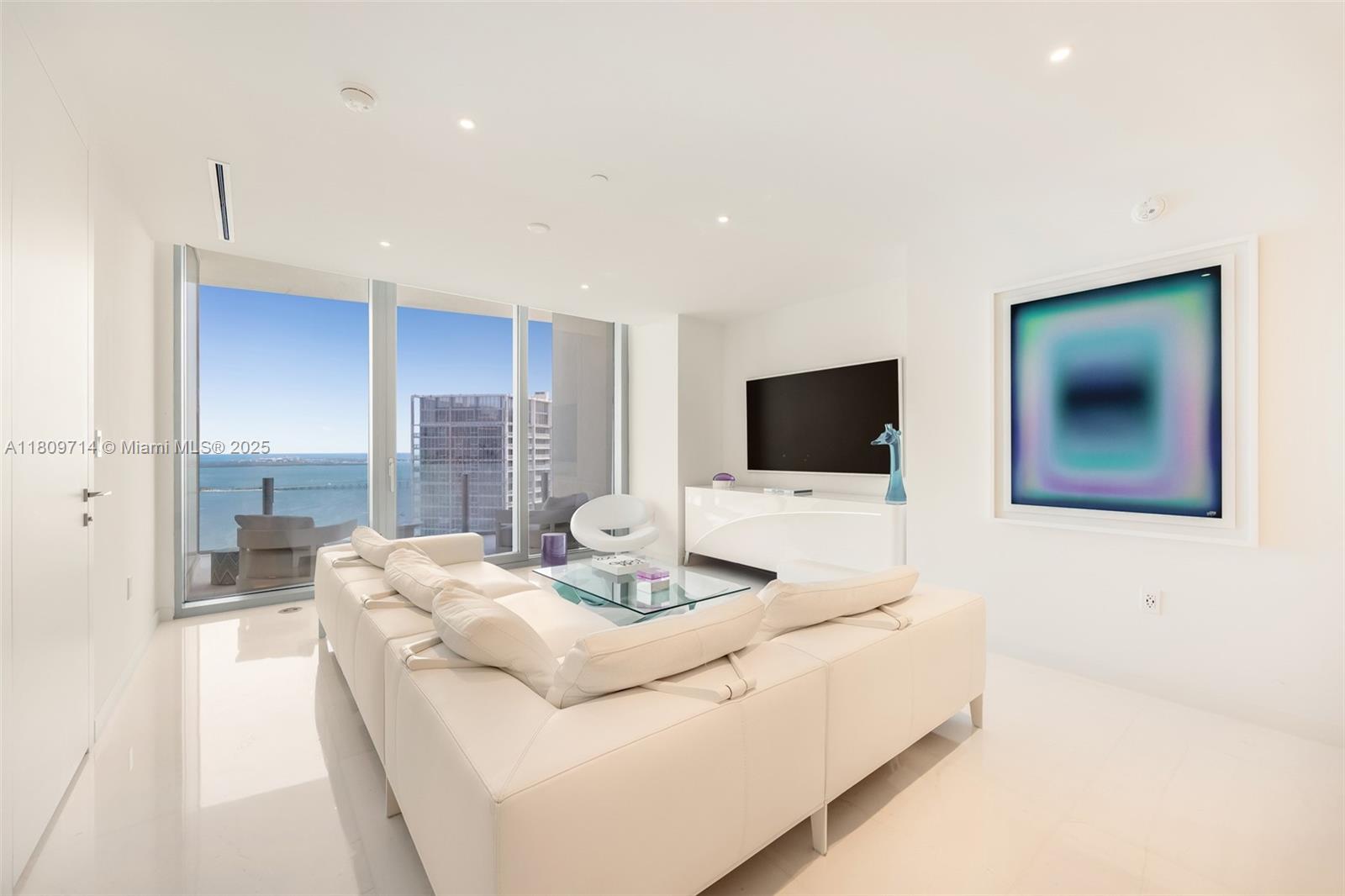 A modern living room features a white sectional sofa, glass coffee table, and floor-to-ceiling windows — 300 Biscayne Blvd Way # 5205W, Miami FL 33131, MIAMI, FL