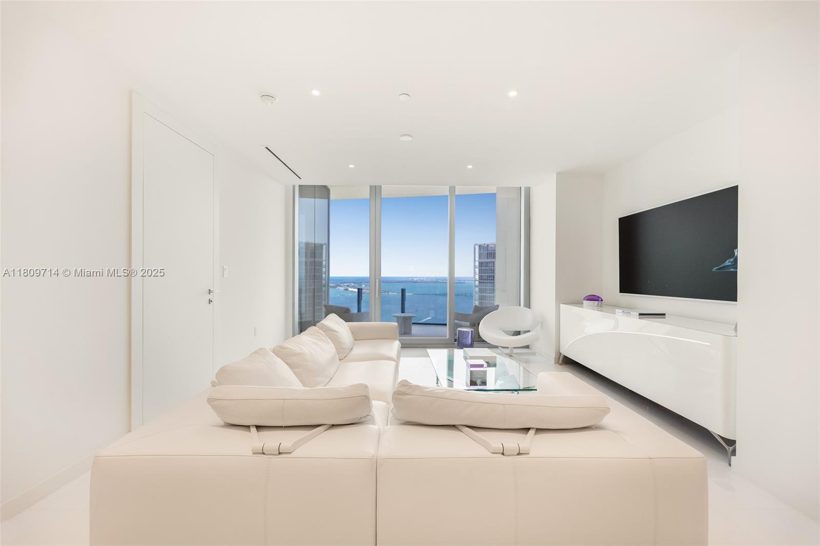 A modern white living room features a large sectional sofa, glass coffee table, and ocean view — 300 Biscayne Blvd Way # 5205W, Miami FL 33131, MIAMI, FL