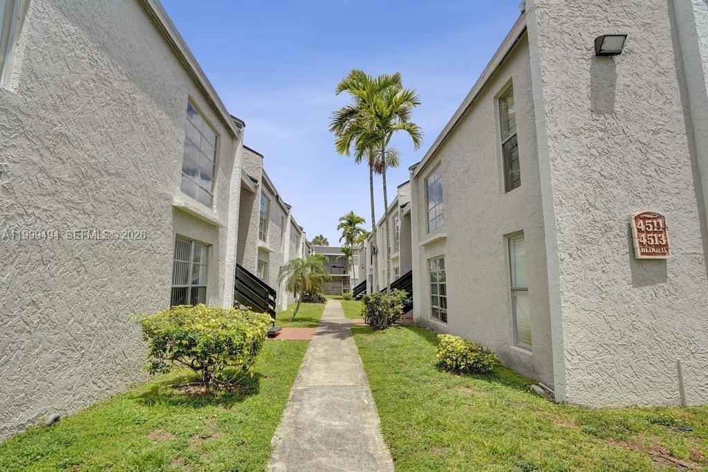 A concrete walkway leads between two multi-story residential buildings with palm trees and landscaping — 4511 Treehouse Ln # B, Tamarac FL 33319, TAMARAC, FL
