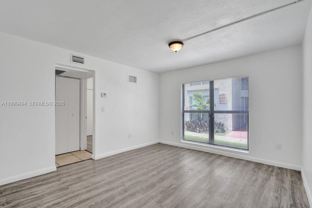 An empty room with white walls, gray wood-look flooring, and a large window — 4511 Treehouse Ln # B, Tamarac FL 33319, TAMARAC, FL