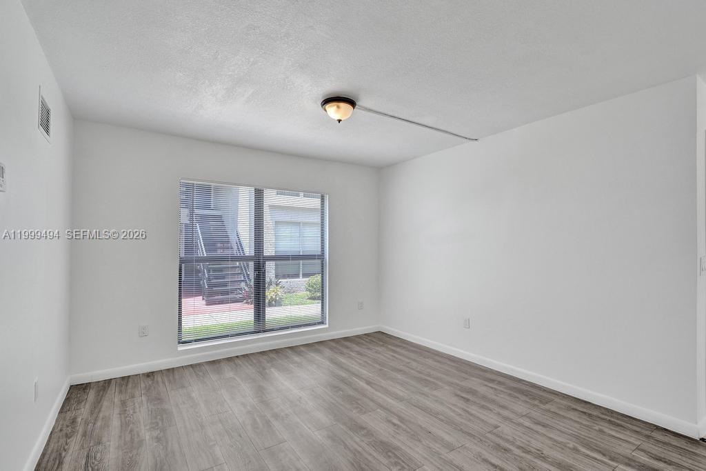 An empty bedroom features white walls, wood-look flooring, a window, and a ceiling light fixture — 4511 Treehouse Ln # B, Tamarac FL 33319, TAMARAC, FL