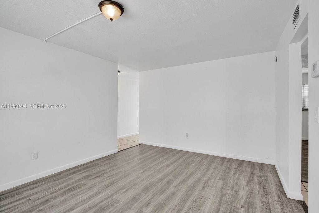 An empty room features white walls, a ceiling light fixture, and grey wood-look flooring — 4511 Treehouse Ln # B, Tamarac FL 33319, TAMARAC, FL