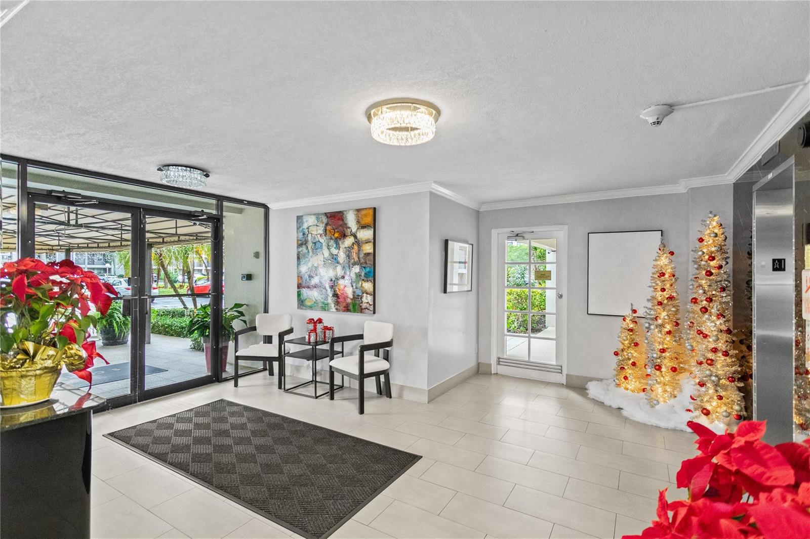 A bright building lobby features tiled floors, two chairs, holiday decorations, and glass entry doors — 3000 S Course Drive # 607, Pompano Beach FL 33069, POMPANO BEACH, FL