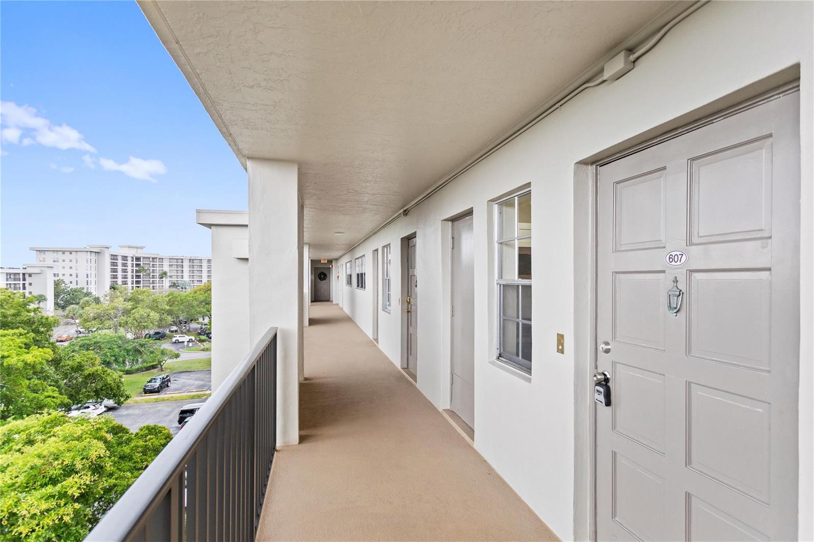 An outdoor apartment building walkway features a row of gray doors and a metal railing — 3000 S Course Drive # 607, Pompano Beach FL 33069, POMPANO BEACH, FL