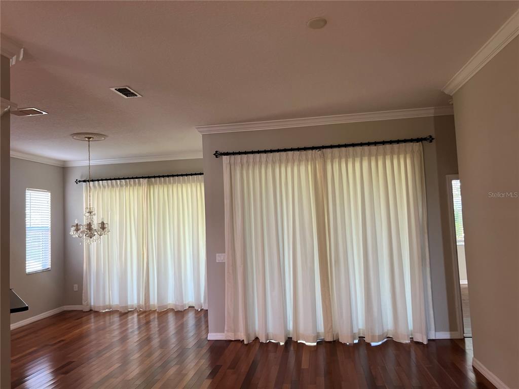 A room with hardwood floors, white curtains, and a chandelier hanging from the ceiling — 119 FALLING ACORN AVENUE, GROVELAND, FL