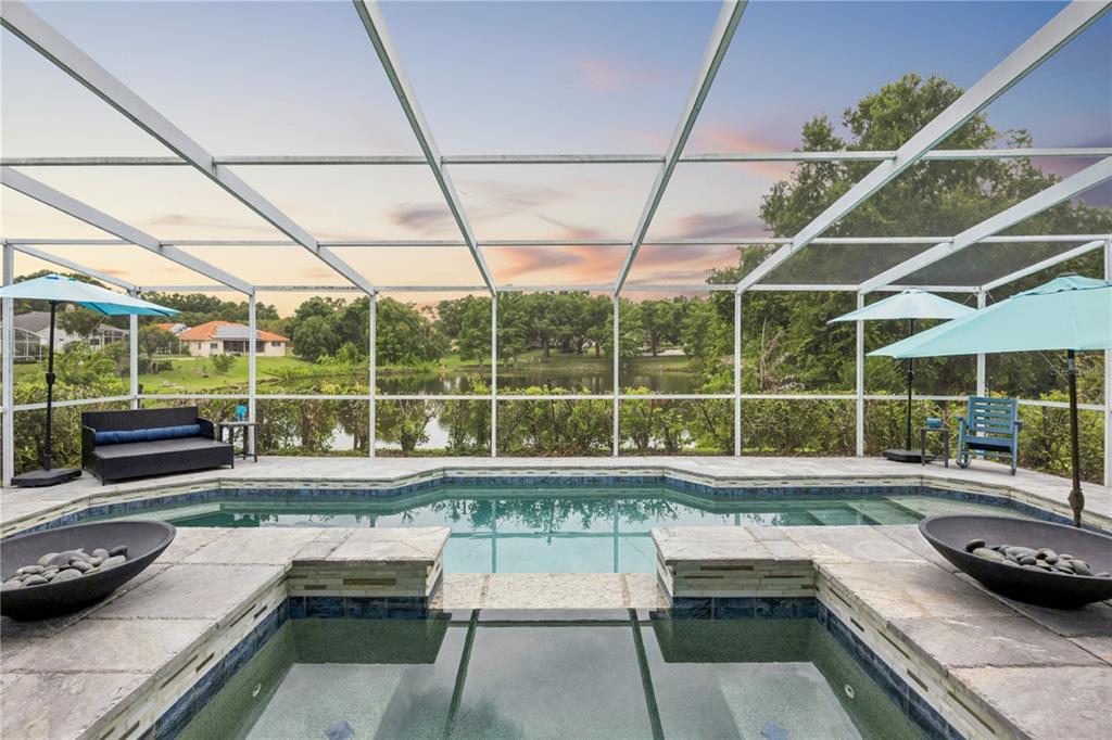 A screened-in pool and spa overlook a lake with a sunset sky in the background — 8606 LOST COVE DRIVE, ORLANDO, FL