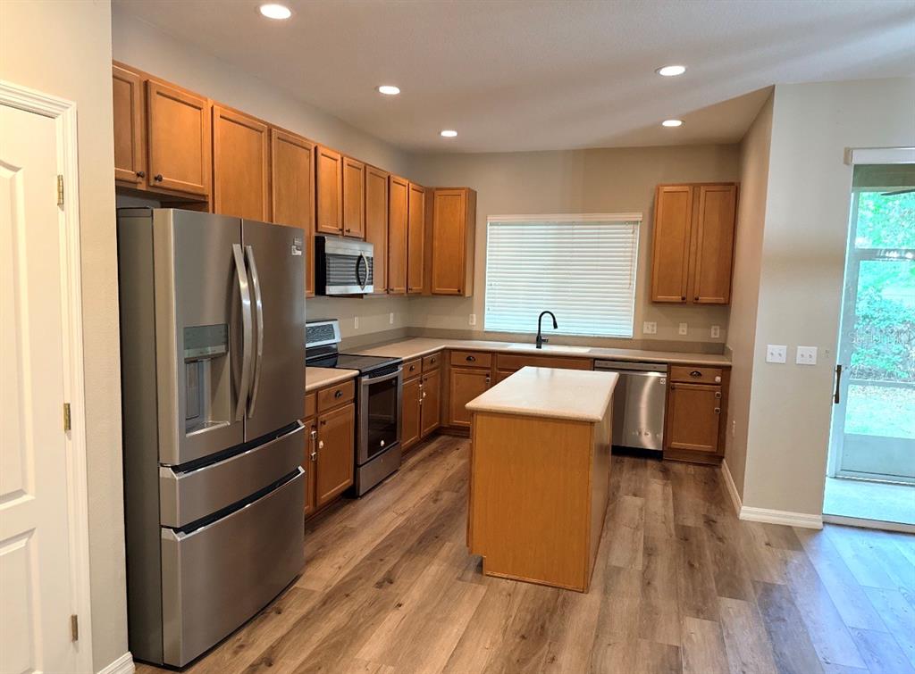 A kitchen features wood cabinets, stainless steel appliances, a center island, and wood-look flooring — 5573 RUTHERFORD PLACE, OVIEDO, FL
