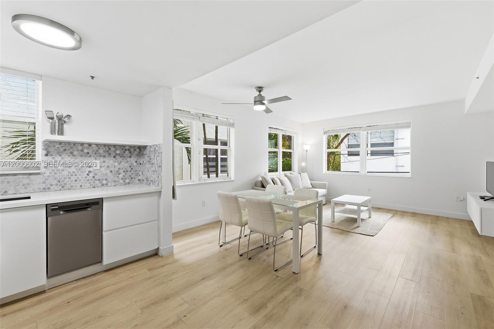 A modern, open-concept living and dining area features white cabinetry, light wood flooring, and windows — 1550 Drexel Ave # 207, Miami Beach FL 33139, MIAMI BEACH, FL