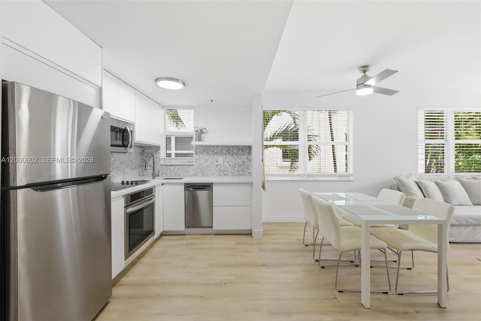 A modern kitchen with stainless steel appliances and white cabinetry opens to a dining area — 1550 Drexel Ave # 207, Miami Beach FL 33139, MIAMI BEACH, FL